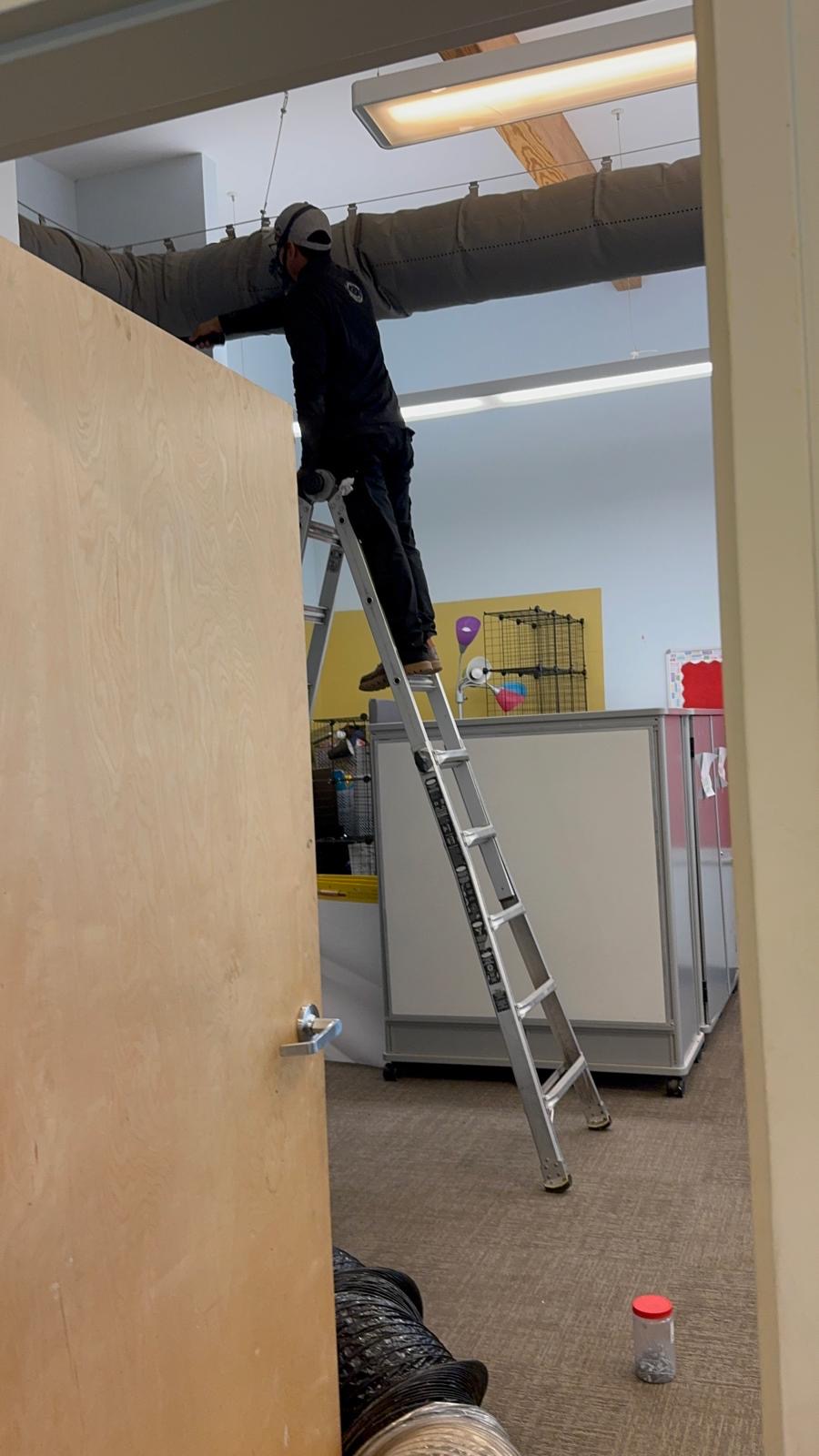 Technician cleaning an insulated ceiling duct run in a commercial building